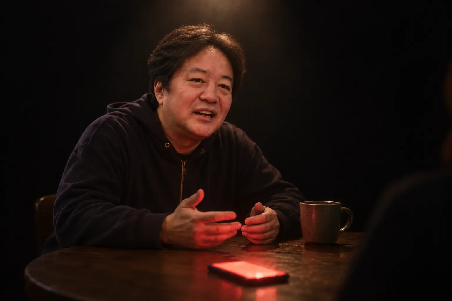 円卓で話す平野。手元のスマホが赤く光っている